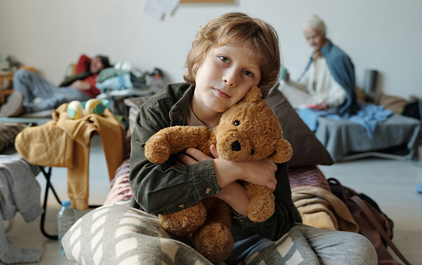 young boy holding teddy bear in messy room with three other people in background