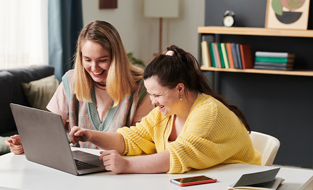 two happy women using a laptop in a bright room enjoying teamwork together three people collaborating on a project