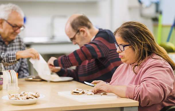 three people preparing food in a kitchen setting while one checks a phone cooking together for four